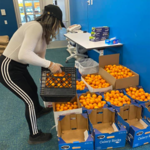 A woman moving a crate with oranges.